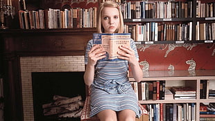 woman sitting on chair beside the book shelf