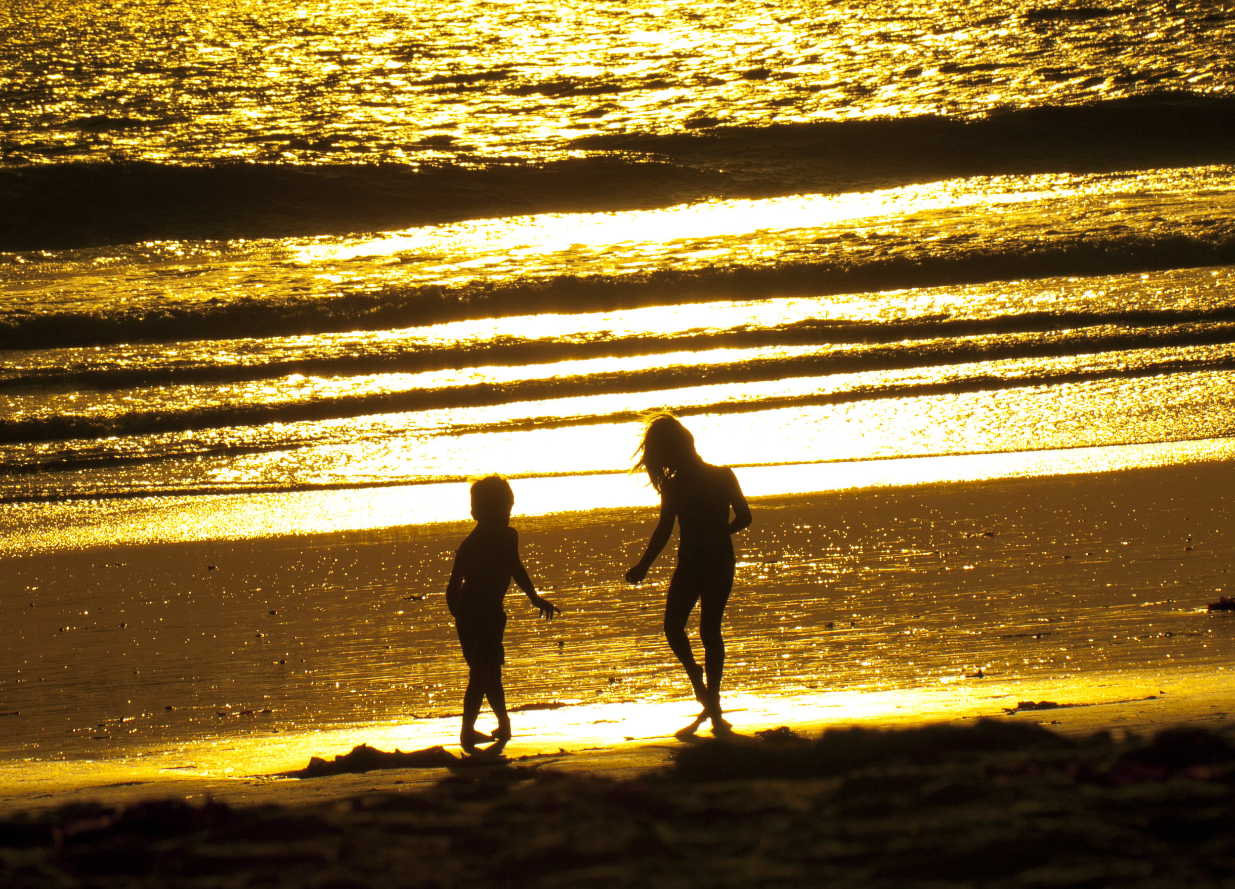 silhouette of two children playing near the seawave