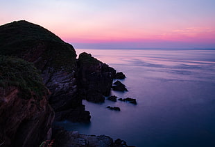 silhouette of rocks near ocean during golden hour HD wallpaper