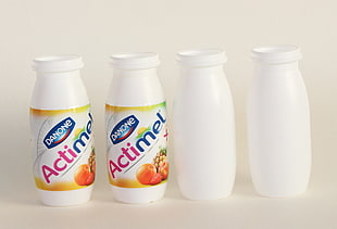 four Actimel plastic bottles on white surface