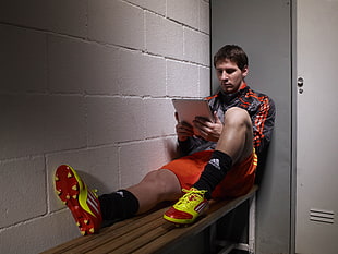 man wearing red-and-green soccer cleats while reading