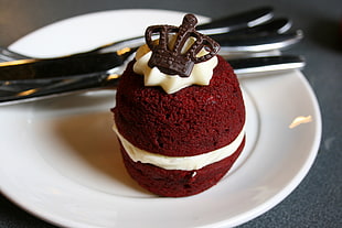 red velvet cake with crown chocolate cookie in white ceramic plate with utensils