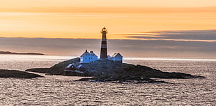white lighthouse near house during sunset
