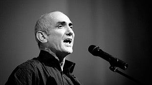 grayscale photography of man in black collared shirt infront of microphone