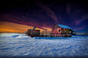 brown wooden house with fence and shed on white ground during starry night
