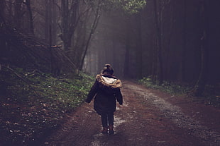girl wearing black jacket walking on road between trees