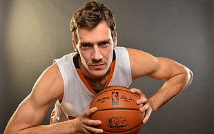 man in white and orange basketball jersey holding basketball looking straight to the camera