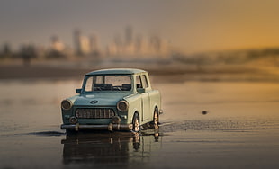 tilt shift lens photo of gray vintage sedan running on seashore during dusk