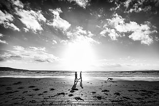 grayscale photo of man and woman near dog walking on seashore