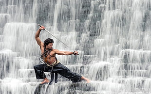 man holding samurai standing near waterfalls during daytime