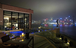 rectangular brown wicker framed glass-top patio table, house, night, lights, cityscape