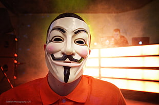 man in orange polo shirt and guy fawkes mask indoors