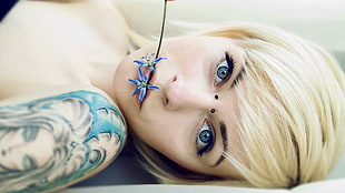 woman with tattoo biting blue petaled flower