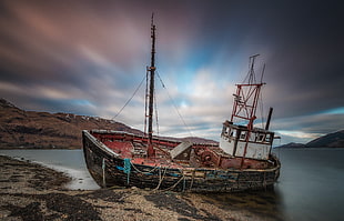 broken sailing ship on beach shore with a view of mountains under blue sky
