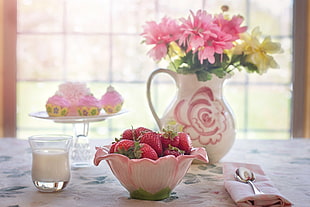 flower on vase, milk on cup, strawberries on bowl and cupcake on stand on top of table