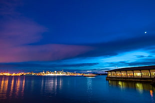 photo of lighted buildings near body of water during night, blue sea