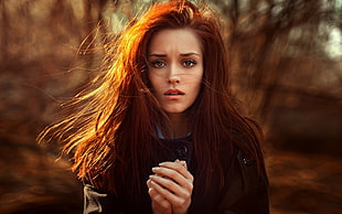 red haired woman in black double-breasted coat holding her hands in bokeh photography