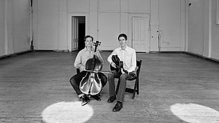 two men holding cello and guitar white sitting on chairs