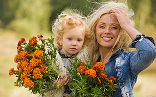 woman and girl holding orange flowers during daytime