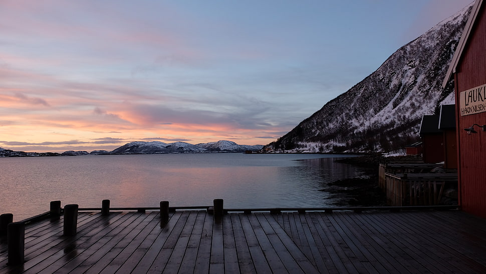 brown wooden dock near sea and mountain during sunset HD wallpaper