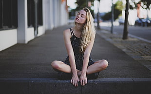 woman wearing black strapless top sitting in gray sidewalk