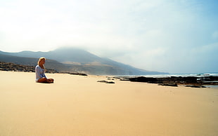 woman sitting on brown sand near seashore