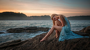 woman sitting on rock near body of wayer