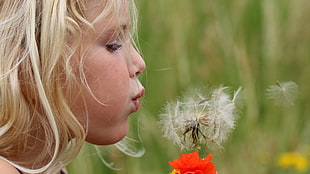 tilt shift lens photography of girl blowing dandelion flower