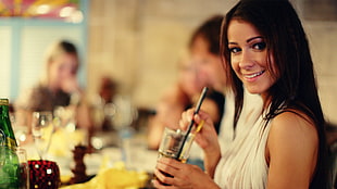 woman wearing white halter top holding drinking glass and black straw while smiling
