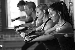 grayscale photo of four people doing exercise using exercise equipment