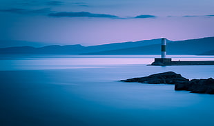 white and gray lighthouse on gray platform in the middle of body of water during dusk, grand marais, minnesota