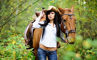 woman in brown hat walking with brown horse
