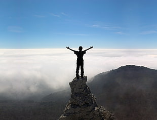 man standing on stone facing mountain rage during daytime
