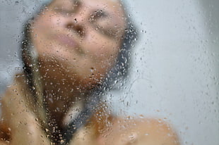 woman taking a bath behind clear glass shower stall with water dews