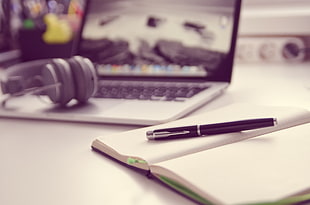 black ball point in white notebook on white wooden table beside MacBook Pro