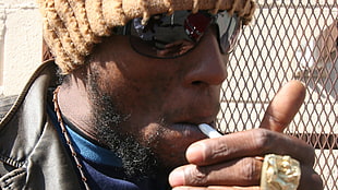 man in brown hat smoking during daytime close-up photo