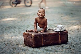 topless baby boy sitting on brown suit case