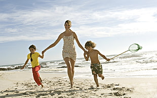 woman holding two boys running on beach shoreline