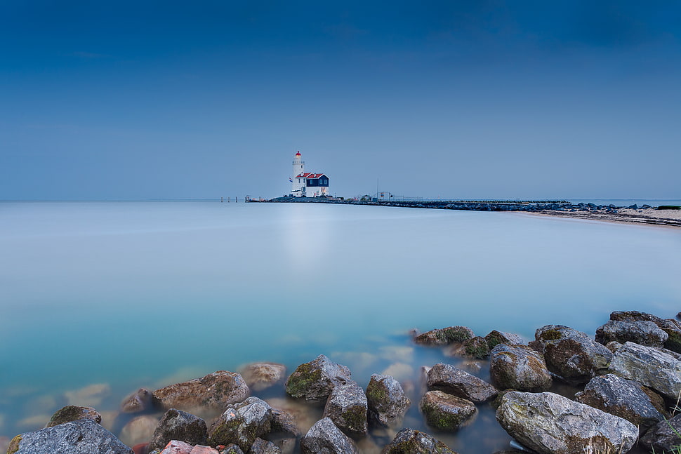 brown stones on shore and a view of a white lighthouse afar under blue sky, marken HD wallpaper