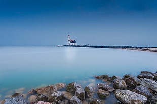 brown stones on shore and a view of a white lighthouse afar under blue sky, marken