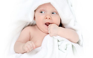 baby covered with white towel while thumb sucking