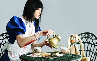 woman holding brass-colored tea pot pouring on teacup in front of plush toy