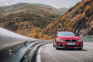 red BMW car park on road near metal rails distance with rocky mountains