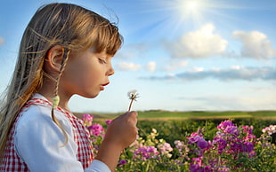 girl holding white Dandelion while blowing during daytime