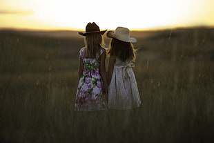 two girls wearing straw hats standing at the middle of green grass field