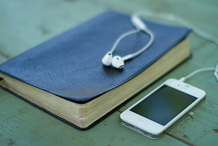 white iPhone 4 near blue hardbound book and EarPods HD wallpaper