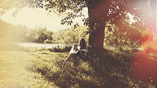 woman playing guitar under tree near lake