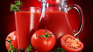 slice of tomato beside glass of tomato juice and pitcher of tomato juice