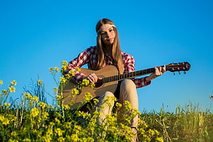 woman in white and red checkered button up shirt playing guitar near yellow flower under blue sky during daytime