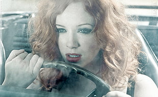 red-haired woman holding black steering wheel;